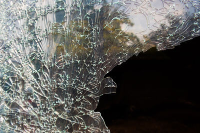 Close-up of broken glass window against black background