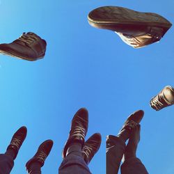 Low section of friends with feet up against clear blue sky