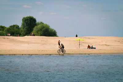 People riding on beach against sky
