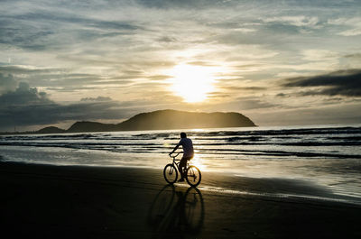 Silhouette man on bicycle at beach during sunset