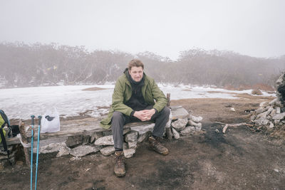 Full length portrait of man sitting against trees during winter