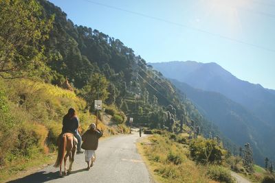 Rear view of man by woman riding horse on mountain road