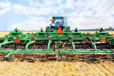 An agricultural tractor with a trailed harrow against the background of a harvested wheat field. 