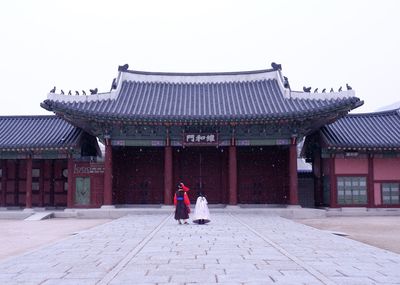 Woman walking by building against sky