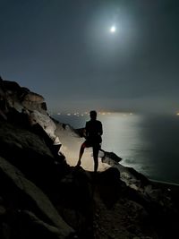 Man standing on rock by sea against sky