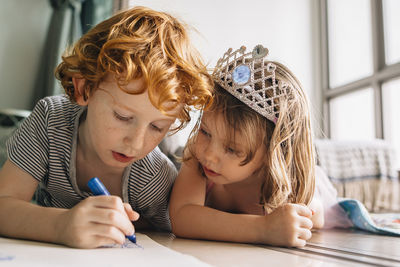 Brother drawing while lying by sister on floor at home