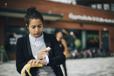 Woman checking time while eating banana at city