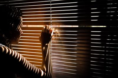 Woman looking through blinds in darkroom