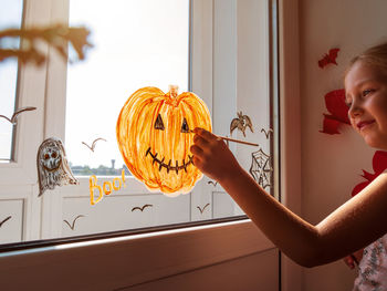 Child painting pumpkin on window preparing to celebrate halloween girl decorates room autumn holiday