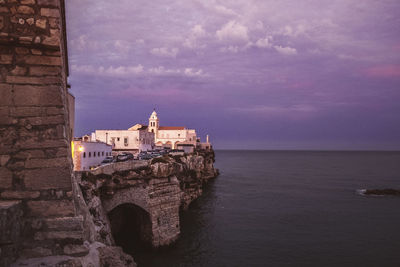 Buildings by sea against cloudy sky