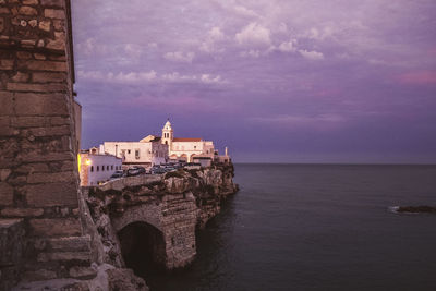 Buildings by sea against cloudy sky