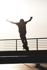 Full length of silhouette man jumping on railing against sky