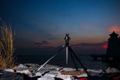 Tripod on rock against sea during sunset