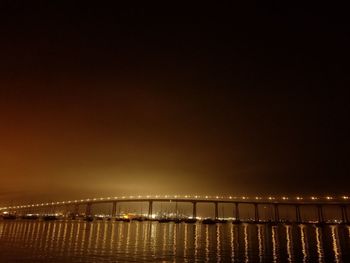 Illuminated bridge over sea against sky at night