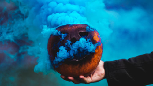 Cropped hand holding jack o lantern emitting blue smoke during halloween