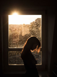 Side view of silhouette woman looking through window