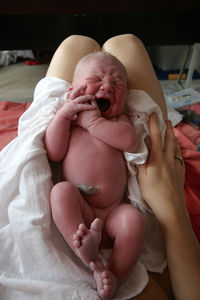 Midsection of mother with naked daughter sitting on bed at home