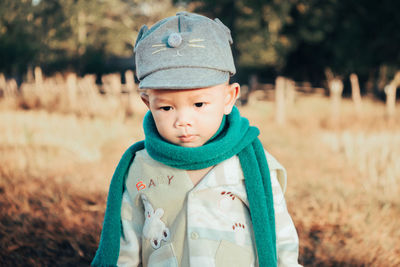 Cute baby boy wearing warm clothing and cap on land