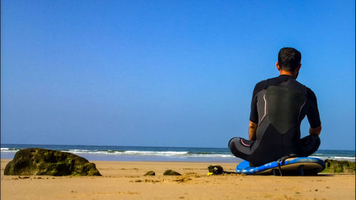 Rear view of man looking at sea against clear sky