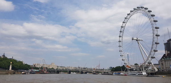 View of ferris wheel in city against cloudy sky