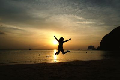 Silhouette person jumping at beach against sky during sunset