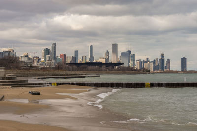 Sea by modern buildings against sky in city