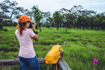 Rear view of woman photographing while standing by railing on grass