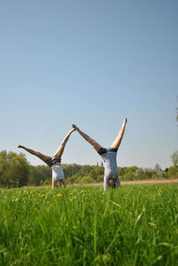 Friends doing handstand on field against sky