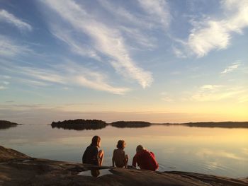 Rear view of siblings at lakeshore against sky during sunset