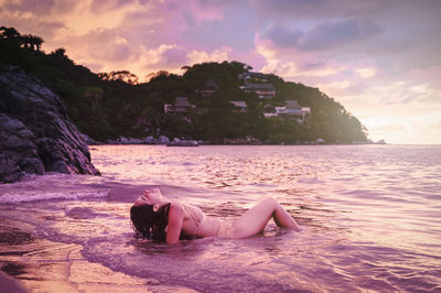 Woman relaxing on beach against sky during sunset