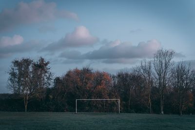 Trees and soccer goal on field against sky at sunset