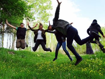 Happy friends jumping on grassy field at park