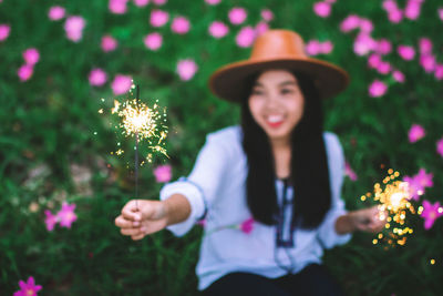 Woman with illuminated sparklers sitting on field at park