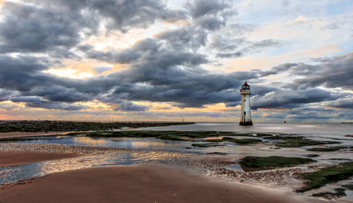 Lighthouse by sea against sky during sunset