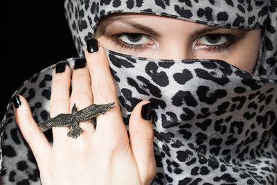 Close-up portrait of young woman with face covered by scarf against black background