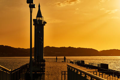 Scenic view of sea with lighthouse orange against sky during sunrise