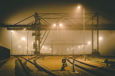 Illuminated railroad tracks by street against sky at night