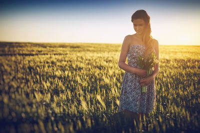 Woman holding bouquet while standing on field against sky