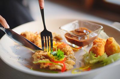 Cropped image of hands cutting fried chicken in plate