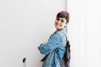 Portrait of smiling young woman standing against wall