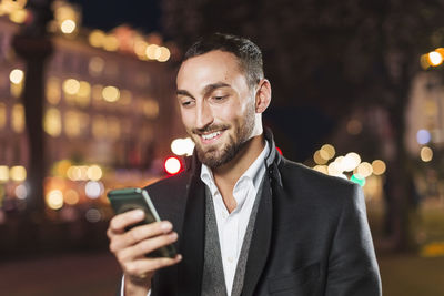 Happy man using smart phone in city at night
