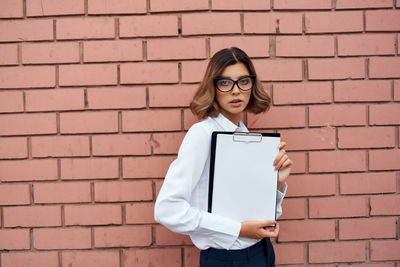 Young woman holding clipboard against wall