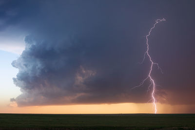 A dramatic lightning strike from an ominous storm cloud over a field in colorado