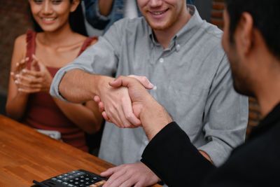 Midsection of colleagues handshaking while woman clapping during meeting