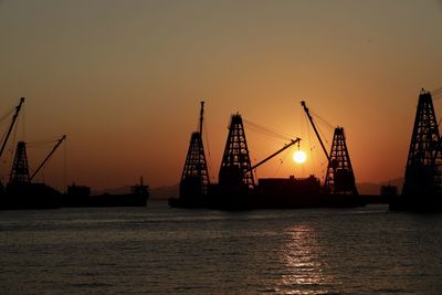 Silhouette cranes at commercial dock against sky during sunset