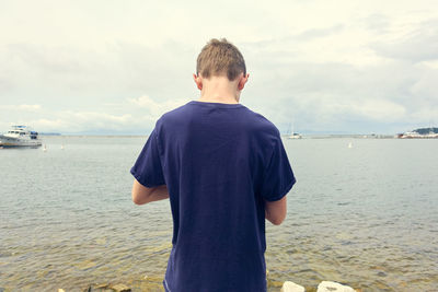 Rear view of boy standing at beach against sky