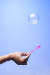 Low angle view of hand holding bubble against blue background