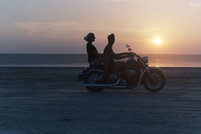 Man riding motorcycle on beach against sky during sunset