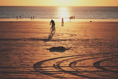Silhouette man riding bicycle on sand against sea at beach