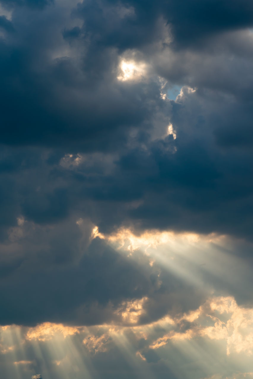 LOW ANGLE VIEW OF SUN STREAMING THROUGH CLOUDS DURING SUNSET